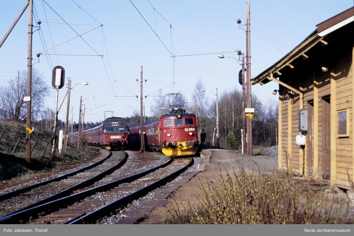 Kryssing på Holstad stasjon mellom hurtigtog fra Oslo S til Halden, tog 153, med elektrisk lokomotiv El 13 2154 og lokaltog til Skøyen med elektrisk motorvognsett type 69