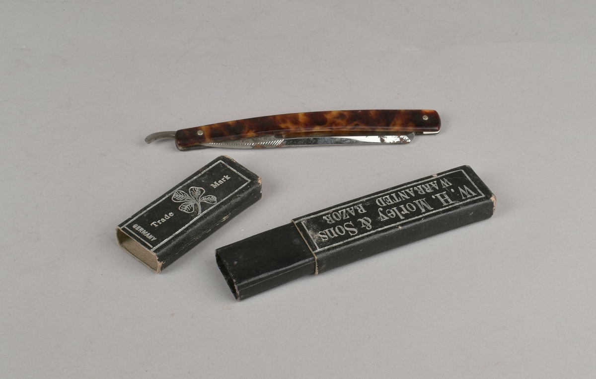 Barberkniv som kan foldes inn i skaftet. Ligger i et todelt pappetui med trykt dekor og skrift.