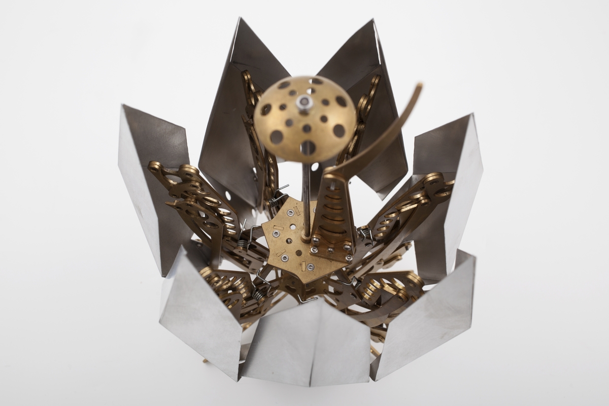 Kinetisk skulptur i messing og aluminium som folder seg ut. Den kan foldes sammen ved å trykke ned midten av skulpturen. Mekanismen minner om en paraply. Sju armer i messing er sentrert rundt en midtdel som står på fire føtter. Hver arm ender i en spiss brettet "skuff" i aluminium.  
Transformer-6.5.01 Pod er fra serien Tribute to the Mars Exploration Rovers.