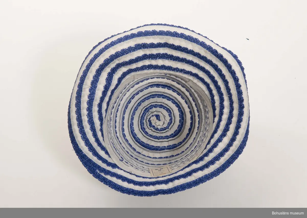 Tillverkad av två slags ripsband, ett blått med uddkant och ett rakt vitt.
Dessa sydda spiralvis från kullens topp och nedåt utåt.