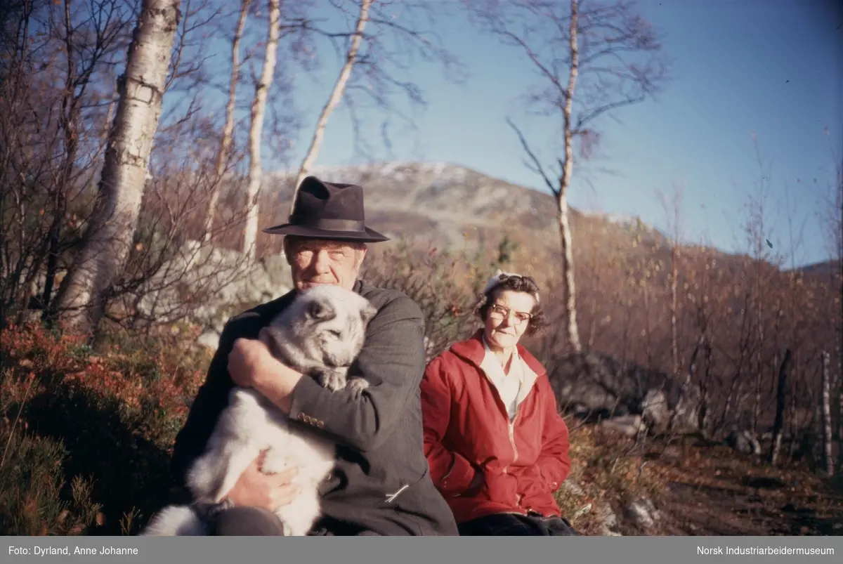 Sigrid og Tor Sanviki sitter i naturen på Nordli, Møsstrond. Mannen iført hatt holder en blårev. I bakgrunn fjell og tær. Kvinne har skaut og lesebriller.