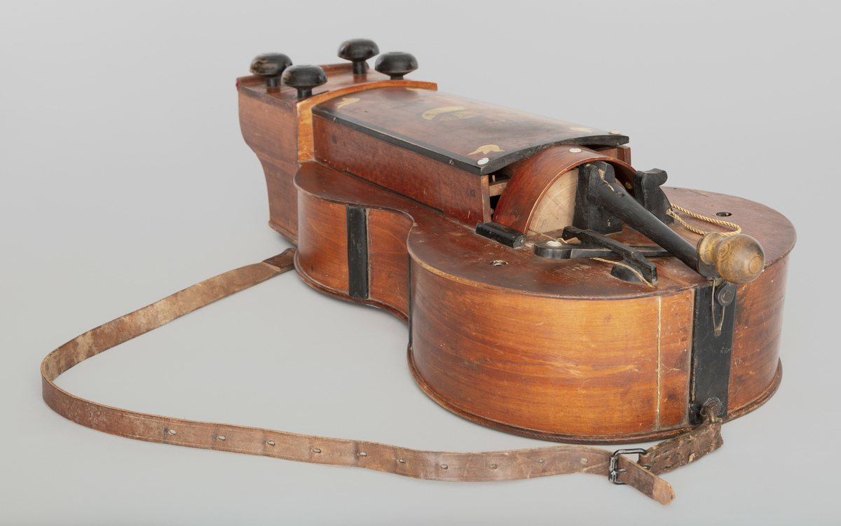 Ungarsk vielle. Bunn og lokk av gran, sarger av løvtre. Gitarform, brunlakkert. 4 strenger, fester til kraftige, sorte treskruer. Tangentkassen dekorert med påmalte, stiliserte, gule blomster. 23 tangenter, sortmalte.