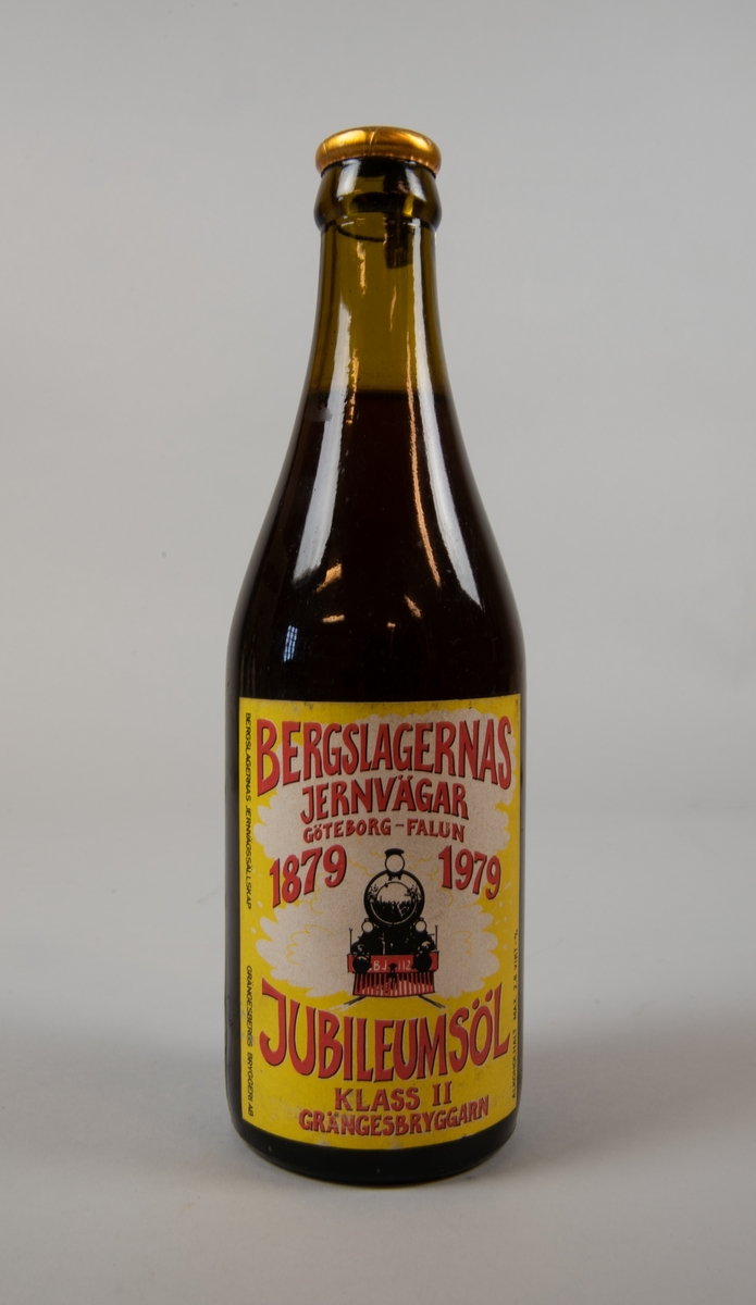 Ölflaska av brunt glas med kapsyl innehållande öl. Flaskan har en etikett med gul botten med vitt i mitten. I nederkanten av det vita är fronten av ett ånglok avbildat i svart och rött. Loket är märkt "BJ 112".

Röd text på flaskan "BERGSLAGERNAS JERNÄGAR GÖTEBORG-FALUN 1879 1979 JUBILEUMSÖL KLASS II GRÄNGESBRYGGARN". Utmed ena sidan av etiketten står det "BERGSLAGERNAS JERNVÄGSSÄLLSKAP" samt "GRÄNGESBERGS BRYGGERI AB" och utmed motstående sida "ALKOHOLHALT MAX. 2.8 VIKT-%".