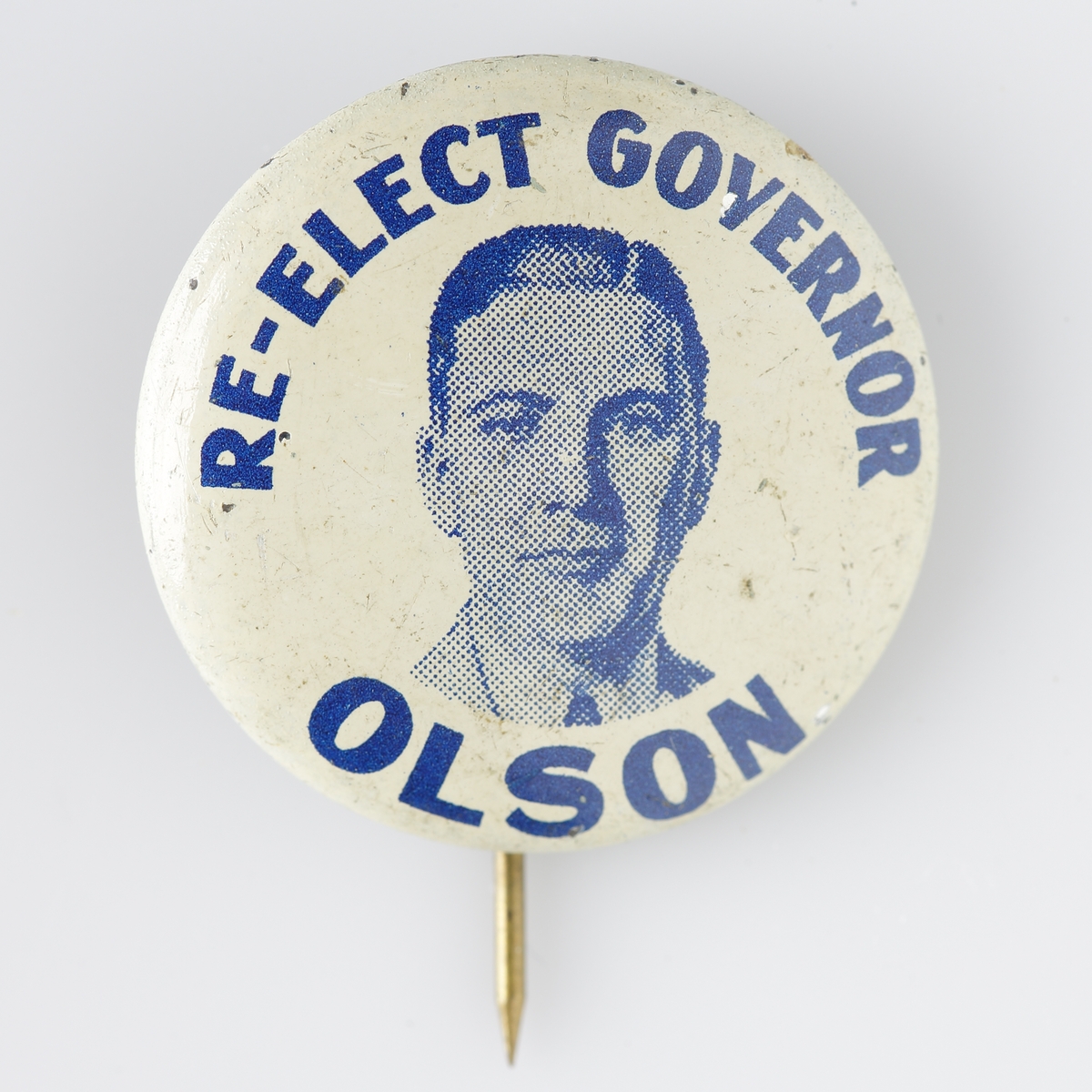 Nålmärke med text "RE-ELECT GOVERNOR OLSON". Amerikansk guvernör i Minnesota vid namn Floyd B. Olsen (1891-1936).