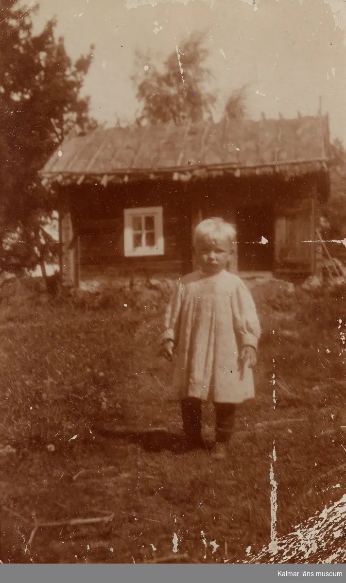 I förgrunden står en pojke i kolt, Curt Nyström Stoopendaal. Bakom honom syns en liten stuga.