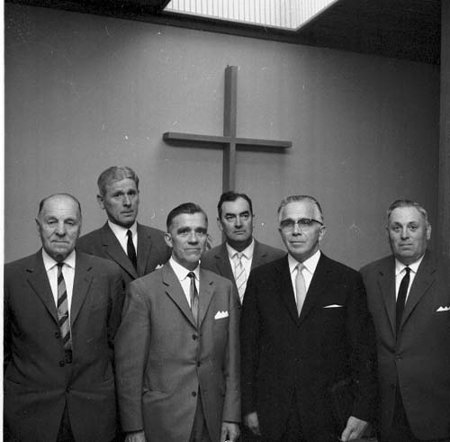 Sex herrar i mörka kostymer och slips står uppställda framför ett kors. Som nr 2 står Rickardsson, som 4 Olofsson och som 5 Svensson.