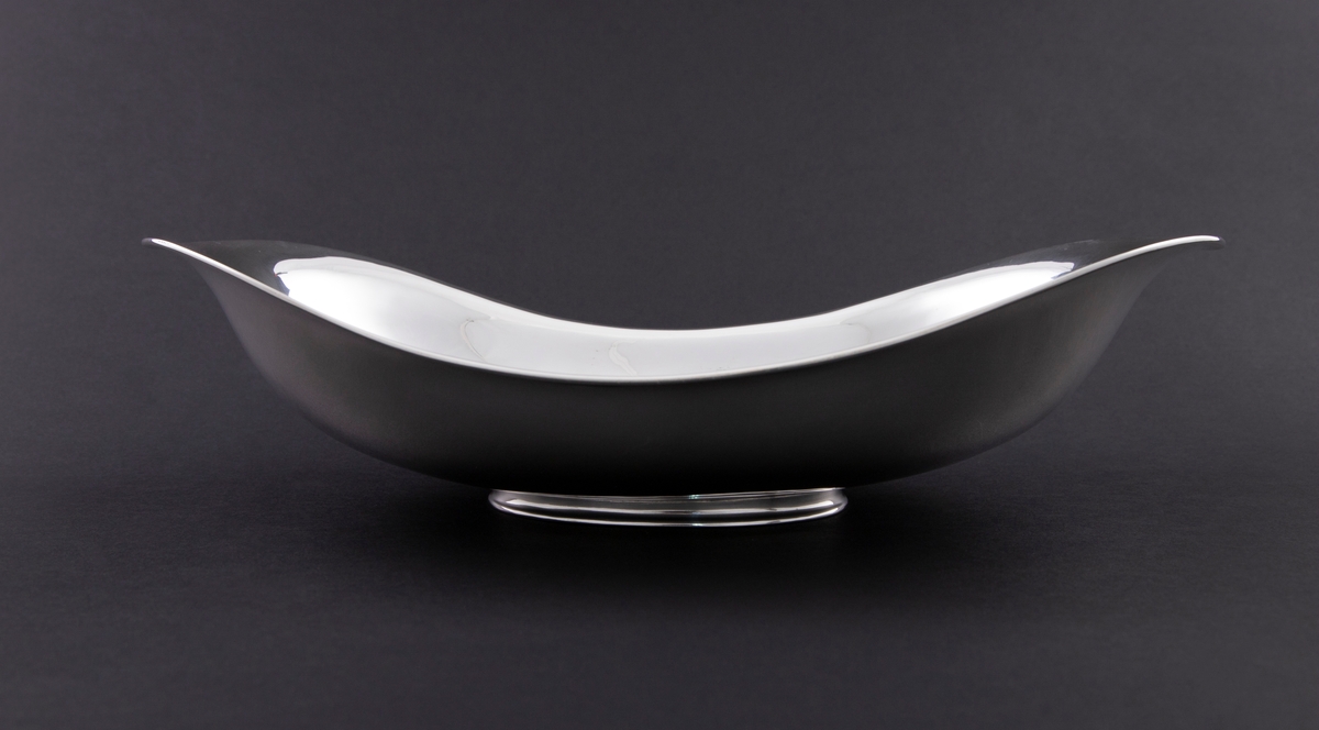 Oval skål i sølv. Langstrakt korpus med mykt buet profil og oppadsvungede sidepartier, som hviler på en lav oval fotring.