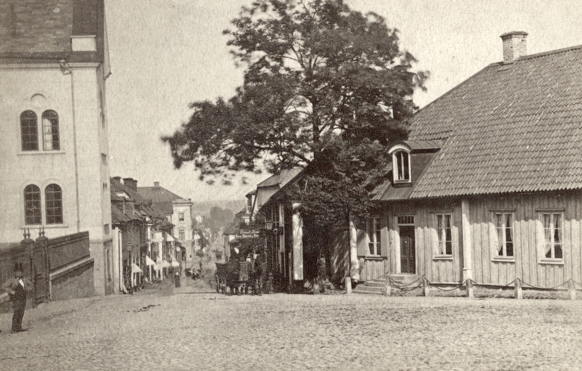 Åldrigt parti av Storgatan i Linköping. Vy från Järntorget österut som genom inslag i bilden kan dateras till sommaren 1875 eller 1876. Närmast till vänster ses en skymt av stadens läroverk, i funktion från 1864. Närmast till höger ligger den så kallade Landskamreraregården.