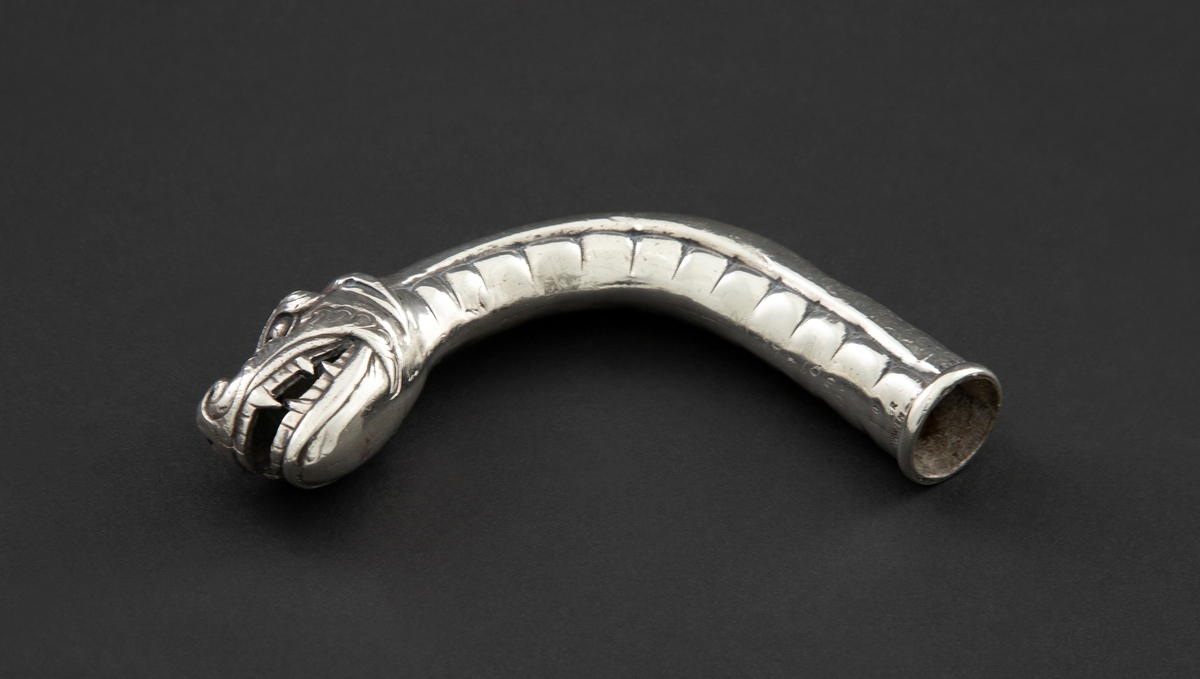 Skafthåndtak til paraply i sølv. Den er støpt, hul og formet som et dragehode med kraftig svungen hals. Halsen danner selve håndgrepet.