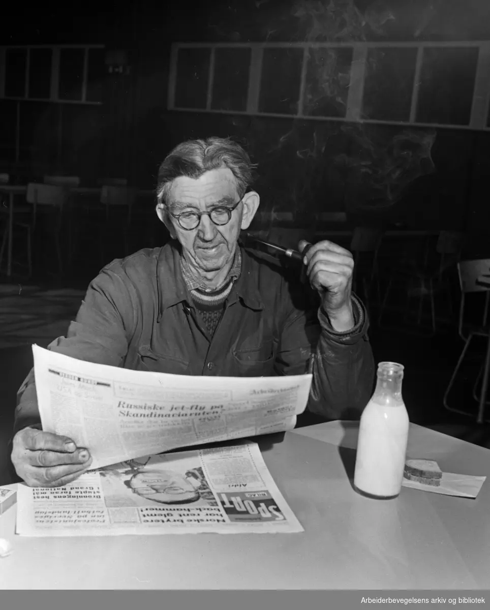 Spisepause. Hjelpearbeider Helge Hansen fra Høvik. Leser avis og røyker pipe. Februar 1956.