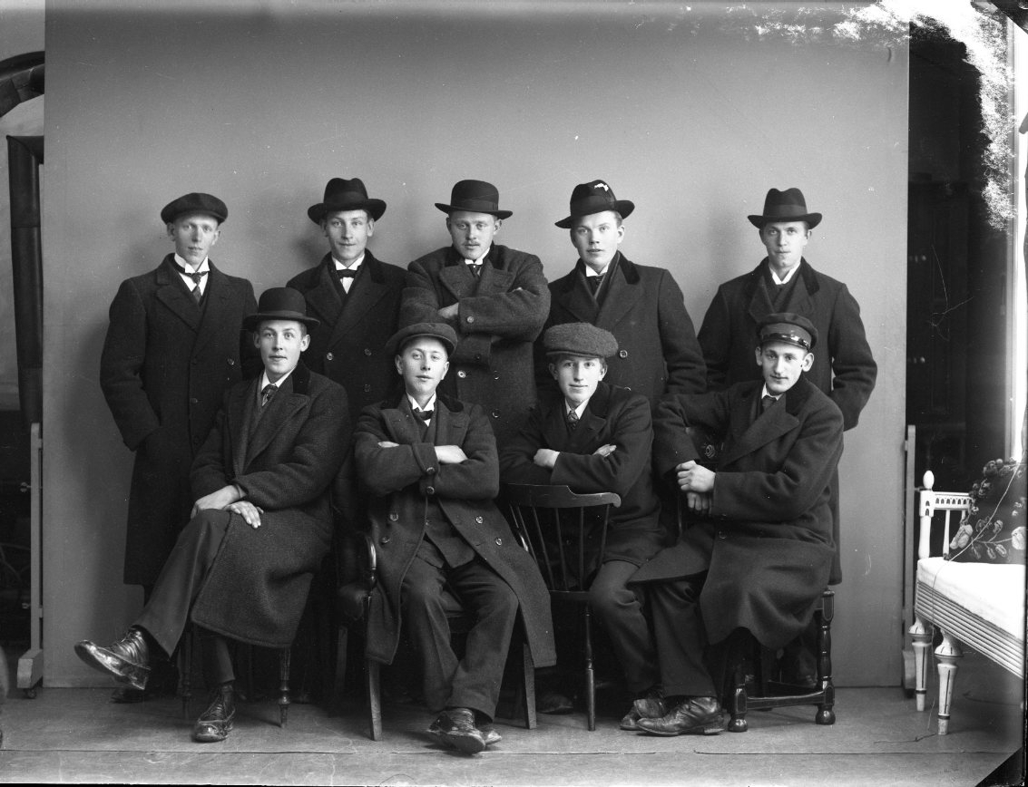 Nio ynglingar i hatt och ytterkläder står respektive sitter. Möjligen en mönstringsbild. En av ynglingarna är Tage Johansson från Lövstaholm, Visingsö.