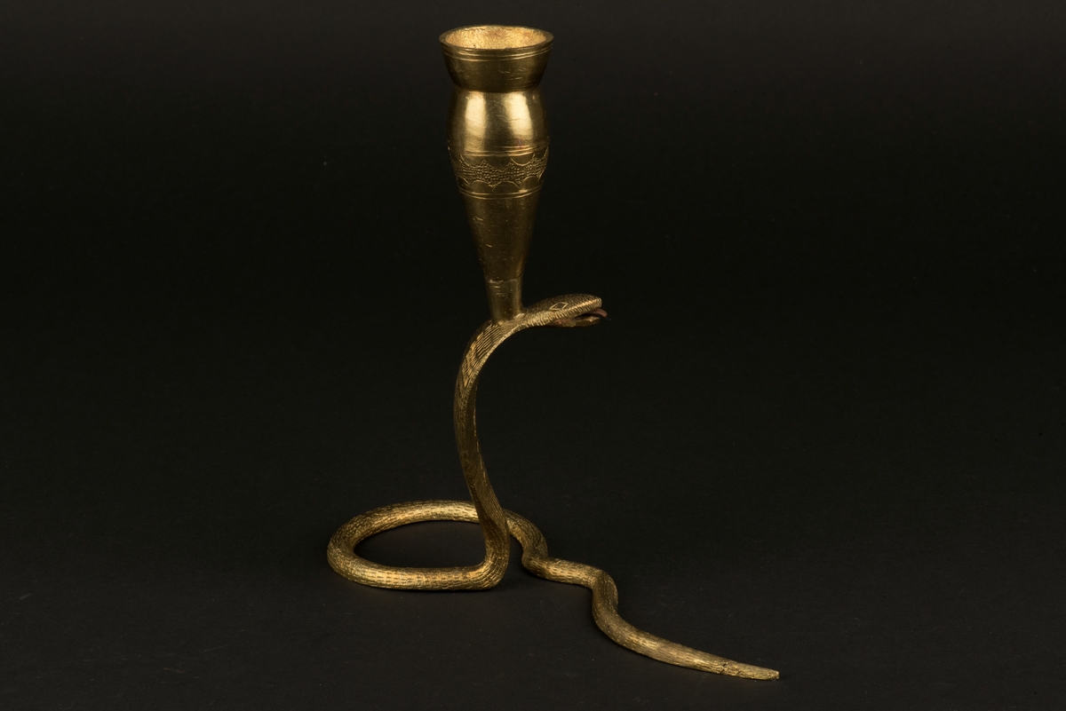 Ljusstake av mässing i form av kobraorm.
Ormens huvud är rest och svansen fungerar som stöd och fot. 
Ljushållaren är fäst på ormens huvud med en skruv.