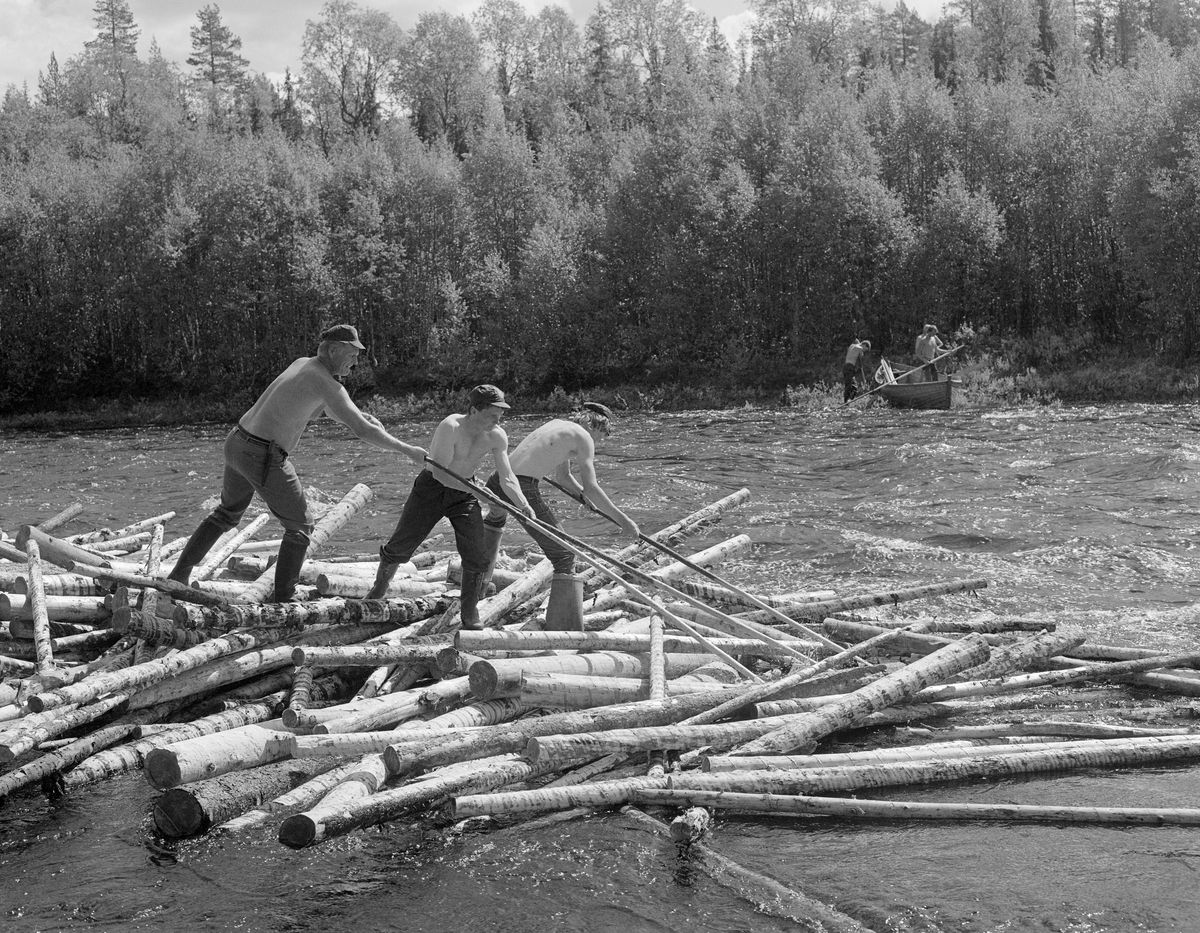 Sluttrensk i elva Stor-Grøna i Trysil, Hedmark. Fløtere i arbeid for å løsne tømmeret i en tømmervase som har bygd seg opp i elva. Båt ved bredden.