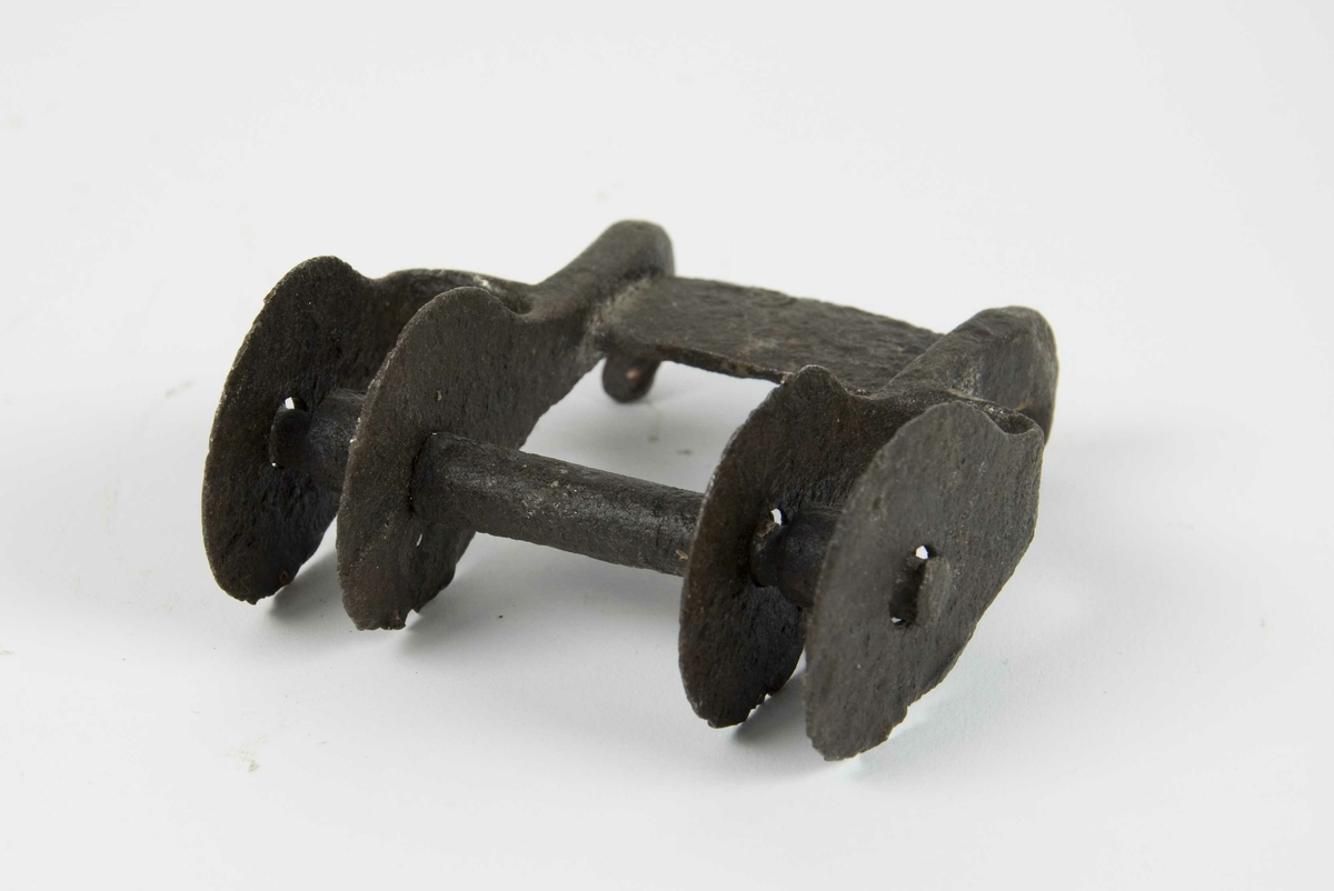 To løpehjul av jern montert på en skaling. Over løpehjulene er det montert en bro med to påsmidde haker for feste av buesnor.
