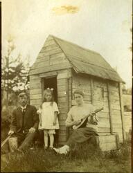 En mann, en jente og en kvinne med mandolin foran et lekehus