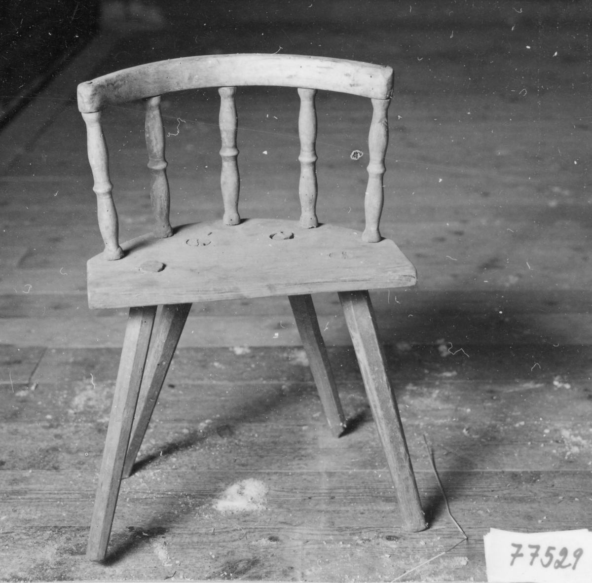 Barnstol med spår av brun målning, nästan halvrund sits med ryggstöd, 5 svarvade pinnar, 4 st intappade och något utällda ben.
