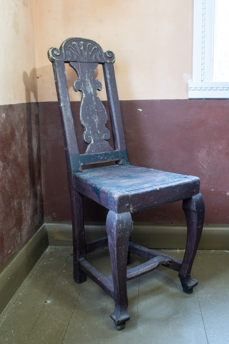 Hjemmelaget stol med rokokko stil og utskjæringer med renessanse preg på ryggen hvor det er rike utskjæringer med et hode. Rødbrun maling.