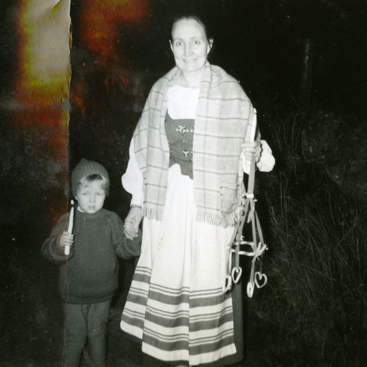 Manne Ekman är på julpromenad tillsammans med mamma Mary i ett mörkt Vommedal cirka 1959. Både Manne och modern håller var sitt tänt ljus i handen. Mary håller även en juldekoration.