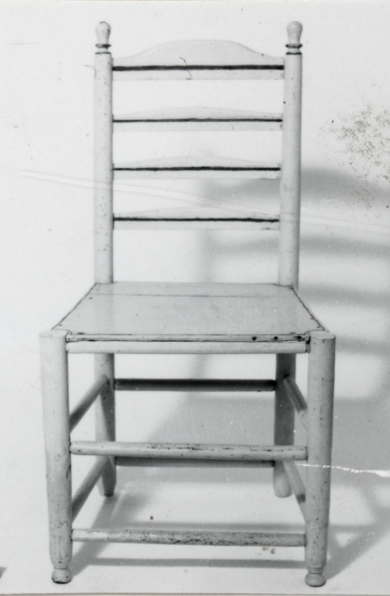 Vitmålad stol sk stegstol med 4 raka svarvade ben. Frambenens avslutningar i form av kulor. Dubbla svarvade tvärslåor. Fastpinnad träsits. Rygg med raka svarvade stolpar upptill avslutas med svarvade knoppar, 4 st tvärslåar, stolen maskangripen.Identisk med inv nr 24481.