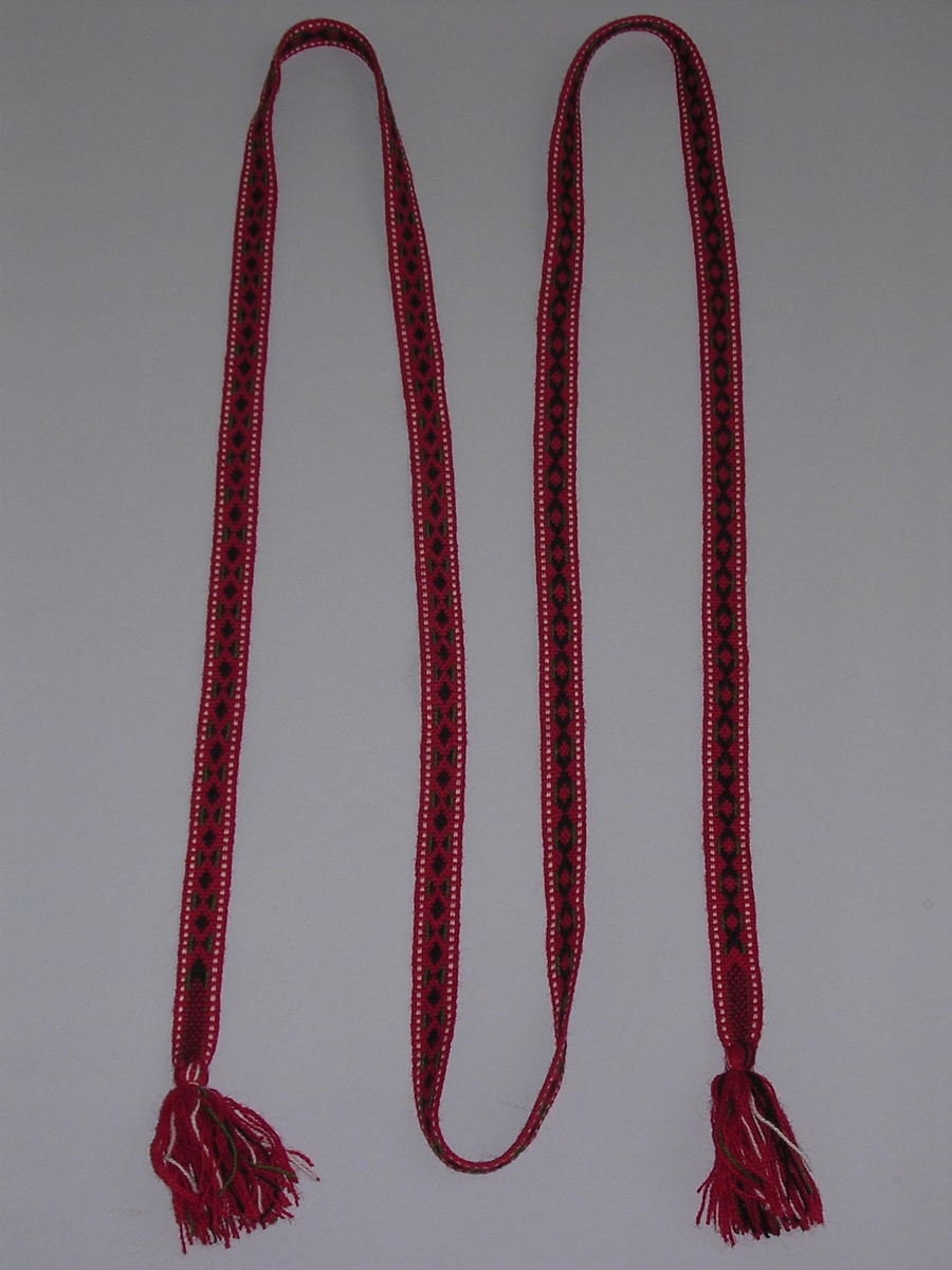 Mönstervävt band, handvävt, i rött, svart, vitt och grönt ullgarn. Tofsar i båda ändar, ca 10 cm långa.

Funktion: Järvsö, Hälsingland