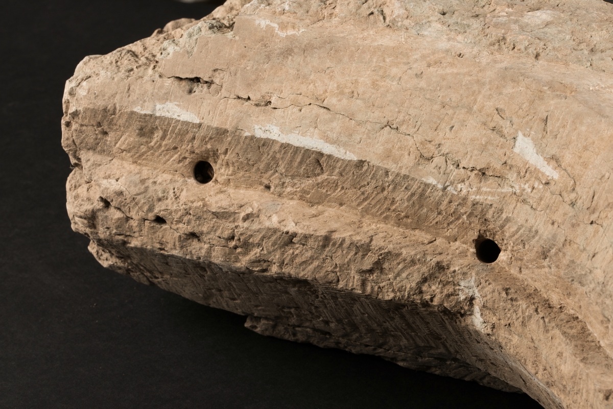Del av masverk tillverkad av huggen kalksten.
Stenen är bevarad i sin fullständiga längd med näsa åt ena hållet. Åt andra hållet finns två avbrutna utskott riktade mot varandra. Uthuggen fals för fönsterbågar.