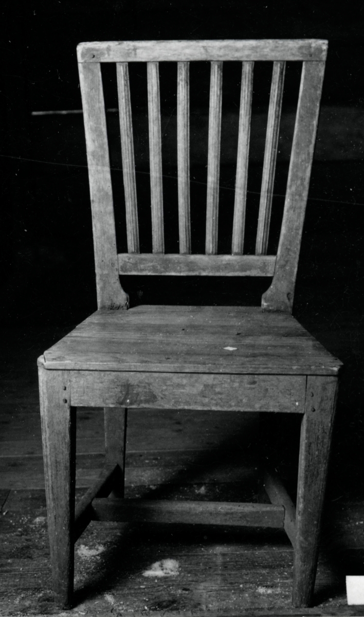 Brunmålad stol med svagt konisk rygg, bredare upptill. 6 st profilhyvlade spjälor, raka 4-sidiga nedåt konade ben,med tvärslå.