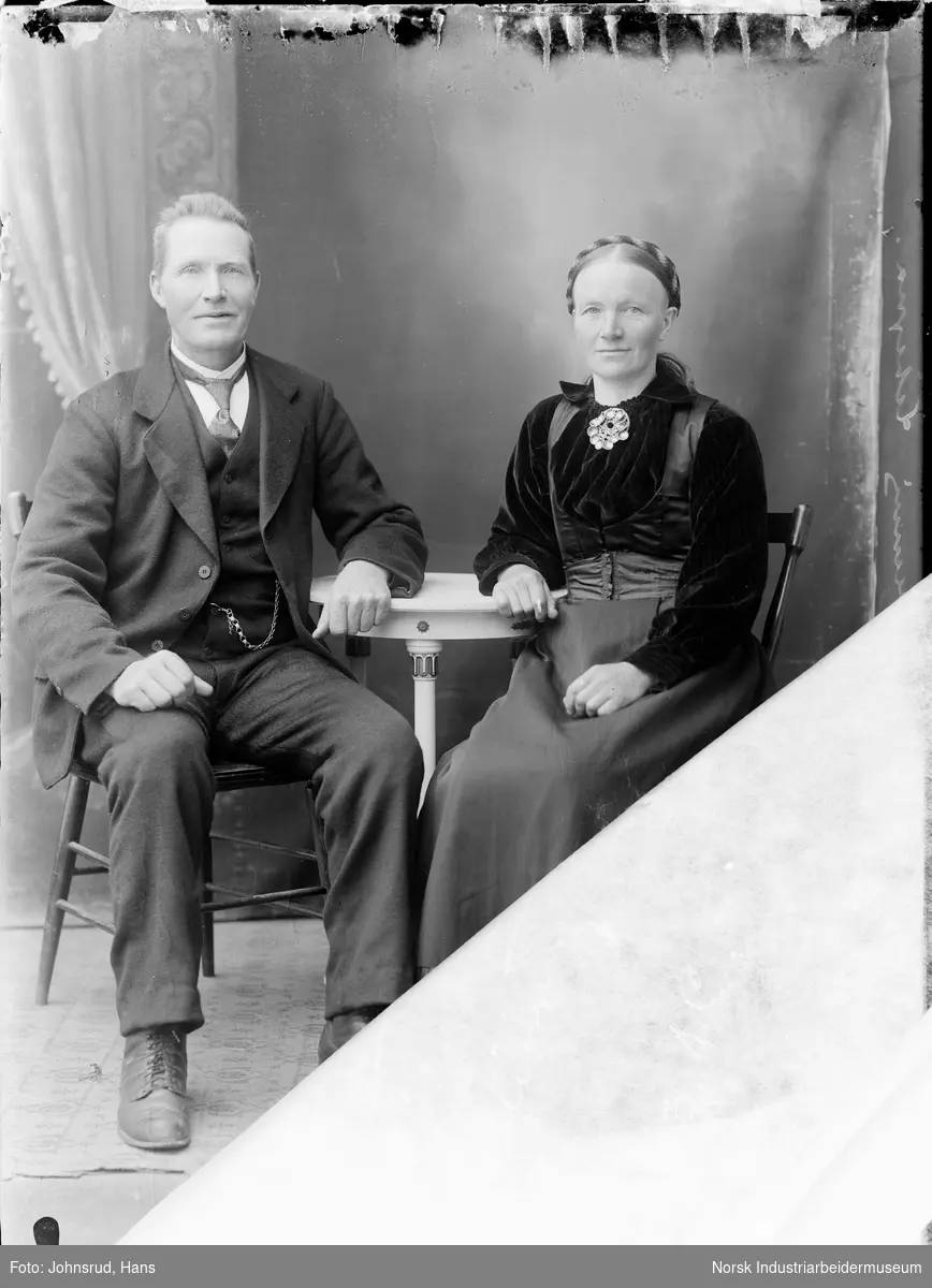 Portrett av mann i dress og kvinne i bunad sittende ved et bord