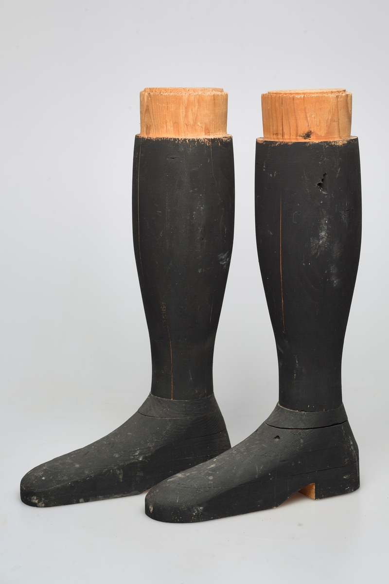 Svarte kompakte støvler av tre for utstilling. De er formet fullstendig etter kroppen og er del av en helfigur av en mann.
