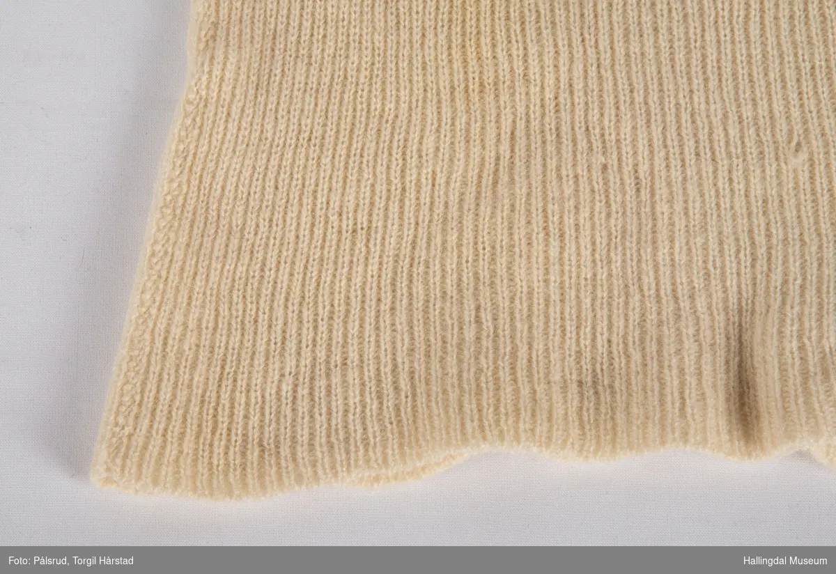 Hvit strikket trøye uten ermer. Ermene er kuttet av. Heklet kant rundt halsåpning.