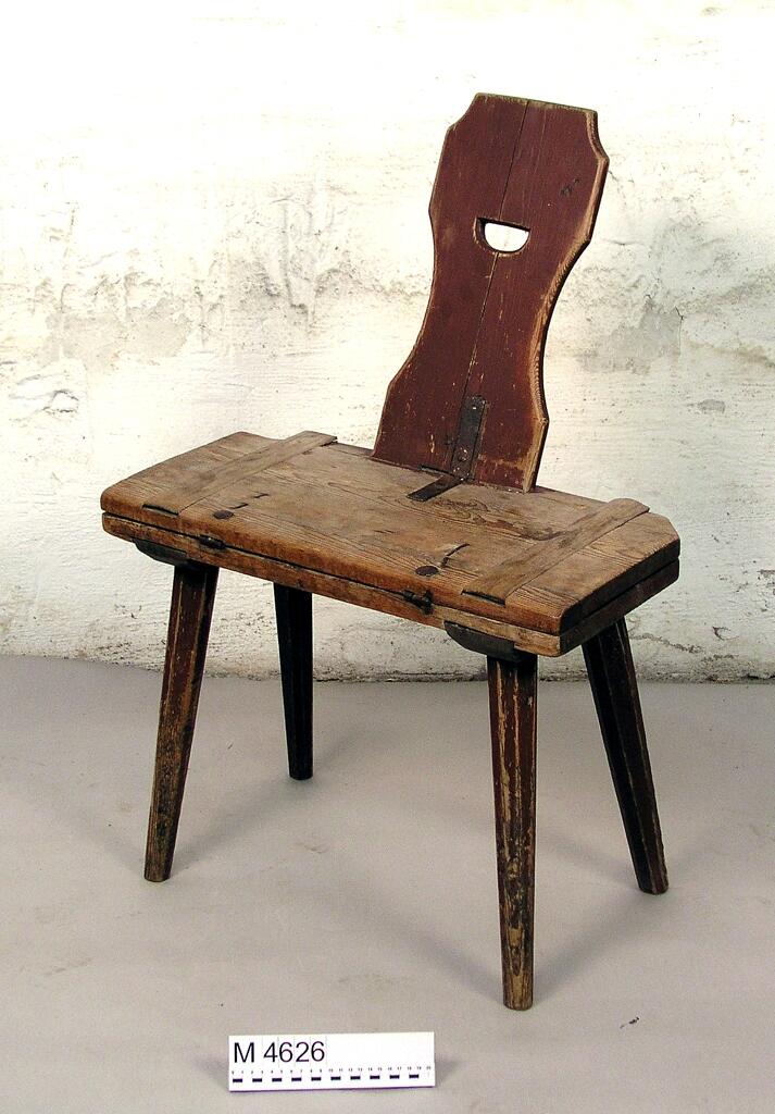 Bordstol, av barrträ. Målad i rödbrunt. Fyra åttkantiga ben. Ryggbrädan profilerad och med halvmånformigt hål. 