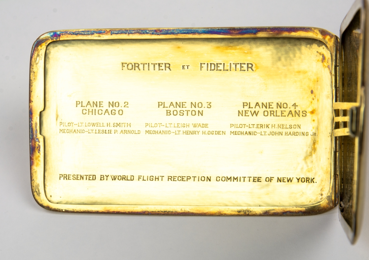 Cigarettetui, på framsidan en relief av ett flygplan och under flygplanet E.H.N. På etuiets baksida en världskarta med flygrouten utmärkt. Ovan kartan texten "ROUND THE WORLDFLIGHT USARMY AIR SERVICR.1924". 
Inuti locket står det FORTITER ET FIDELITER. PLANE NO.2 CHICAGO PILOT-LI.LOWELL H. SMITH MECHANIC-LT.LESLTE P. ARNOLD.PLANE NO.3 BOSTON PILOT- LT.LEIGH WADE MECHANIC- LT.HENRY H. OGDEN.PLANE NO 4 NEW ORLEANS PILOT-LT.ERIK H.NELSON MECHANIC-LT.JOHN HARDING JR Presented by World Flight Reception Committe of new york. 
På andra insidan av locket är sex av flygarnas autografer inristade.