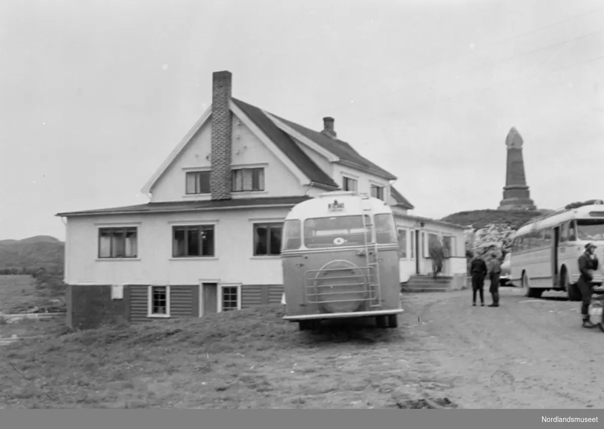 Saltstraumen turisthotell. 2 busser og 3 personer foran hotellet. Ellers minnestøtta til Kong Oscar II's besøk på høyden til høyre.