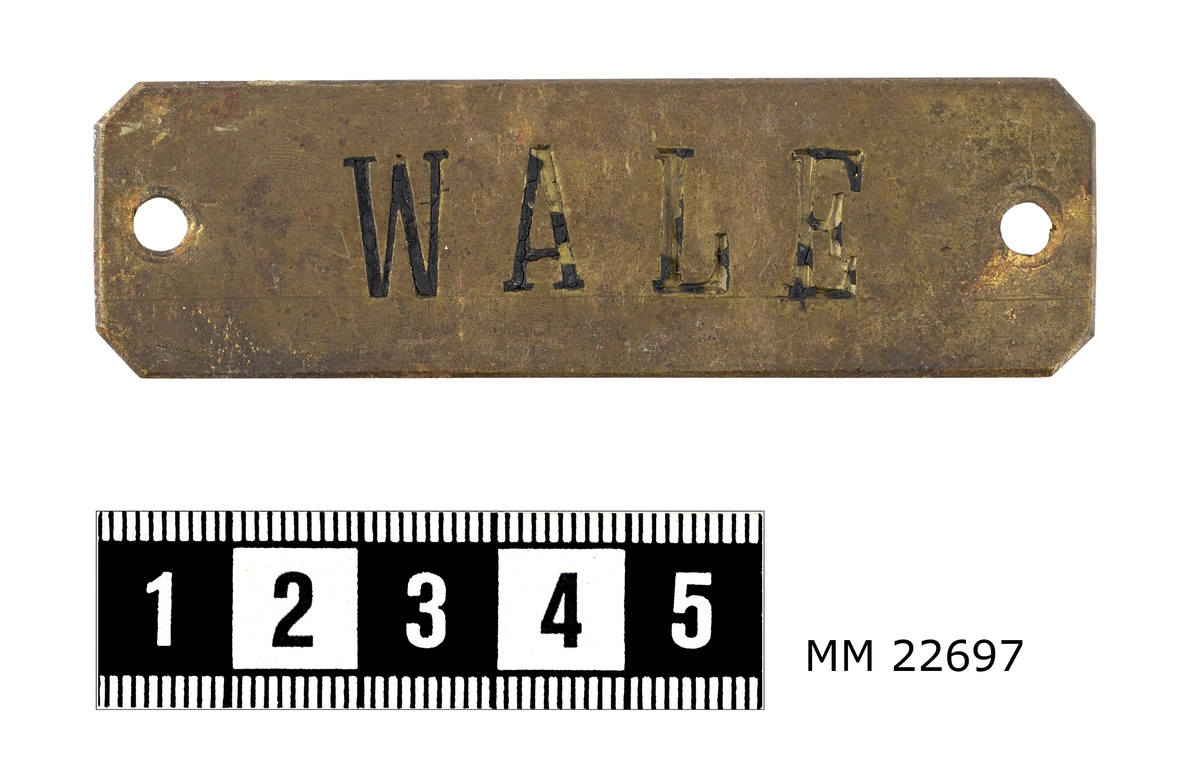 Skylt av mässing, rektangulärt format, avskurna hörn.
På framsidan text: "WALE".
Hål i vardera kortsida.