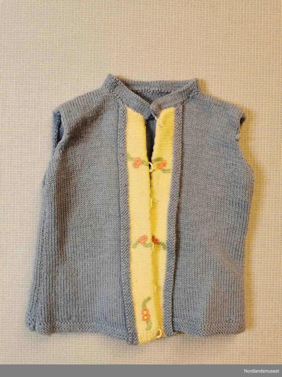 Blå strikket jakke til barn. Ermene og knappene er fjernet. Broderte blomster langs midten av jakka.