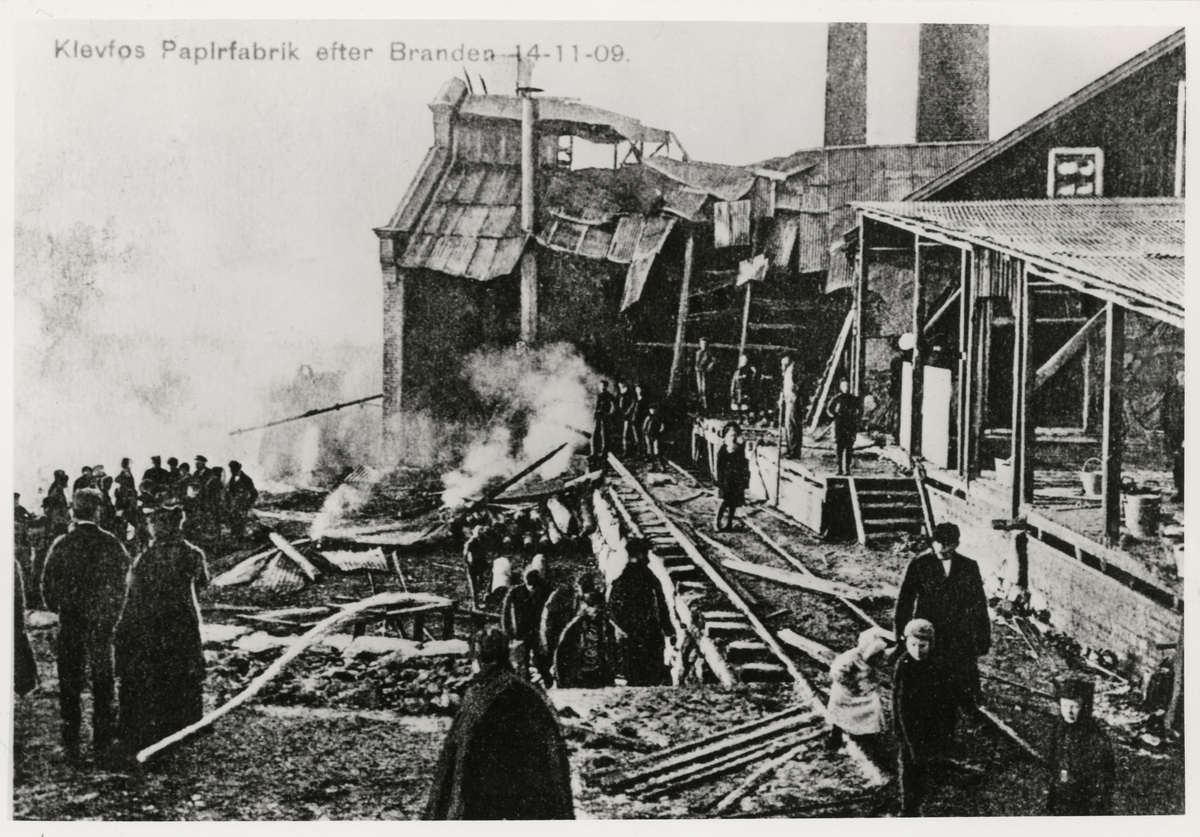 Reproduksjon av et postkort påtrykt teksten "Klevfos Papirfabrik efter Branden 14-11-09". Brannen ved Klevfos Cellulose- & papirfabrik A/S i november 1909.