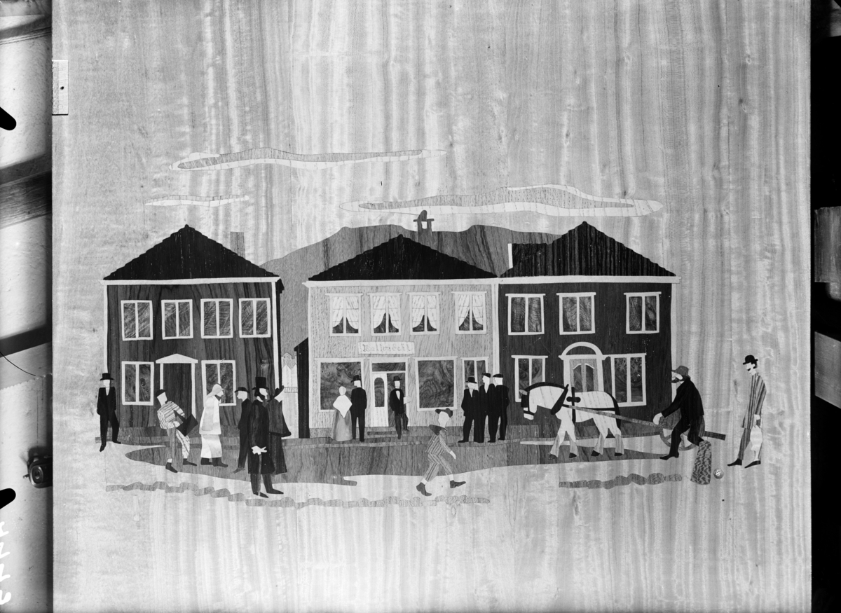 Bilde på treplate med dekor i intarsia, motivet er en bygate med mennesker, hus, butikker og en hest fra "gamle dager". Publisert i Bonytt, trolig 1949-55.