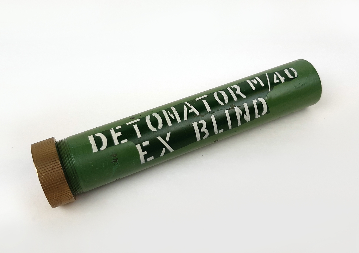 Detonator m/40, blind. Bestående av en grönmålad cylinder i metall med skruvbart lock. Märkt vid sidan: "DETONATOR M/40 EX BLIND".