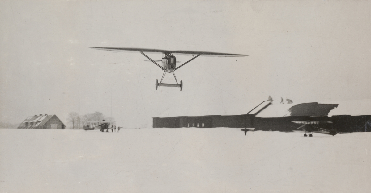 Flygplan FVM J 23 flyger på låg höjd över flygfältet på Malmen, vintertid 1924

Text vid foto: "J. 23, 185 HK. B.M.W. 210 km /tim. 1924."