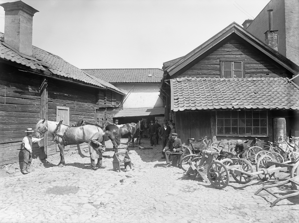 Gårdsinteriör från Stenhusgården, Storgatan 56 i Linköping. Vid tiden bedrev smeden Carl Johan Hall sin verksamhet på gården. Här skoddes hästar och lagades vagnar, den nya tiden representeras av att även cykelreparationer utfördes.