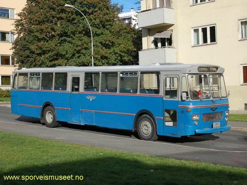 Blå buss med grått tak. Bussens interiør består av blå seter og hyller for oppbevaring over setene. 