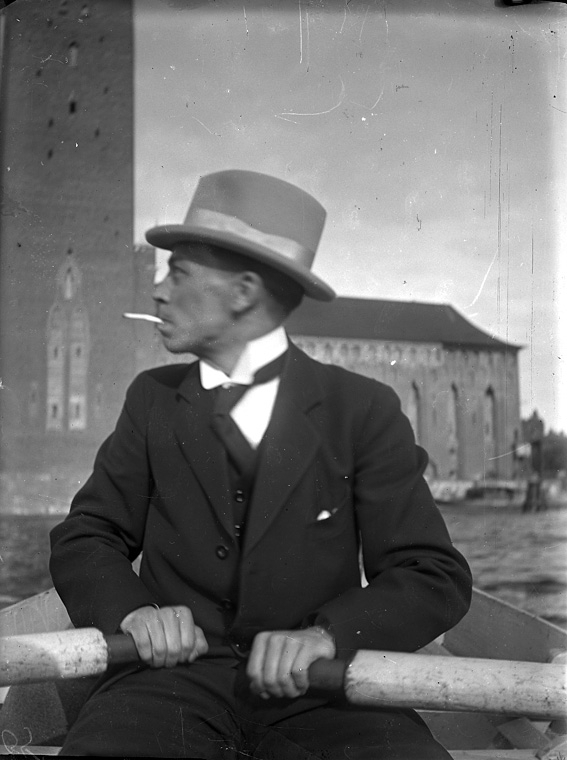 Man i kostym och hatt vid årorna i roddbåt på Riddarfjärden, Stockholm.