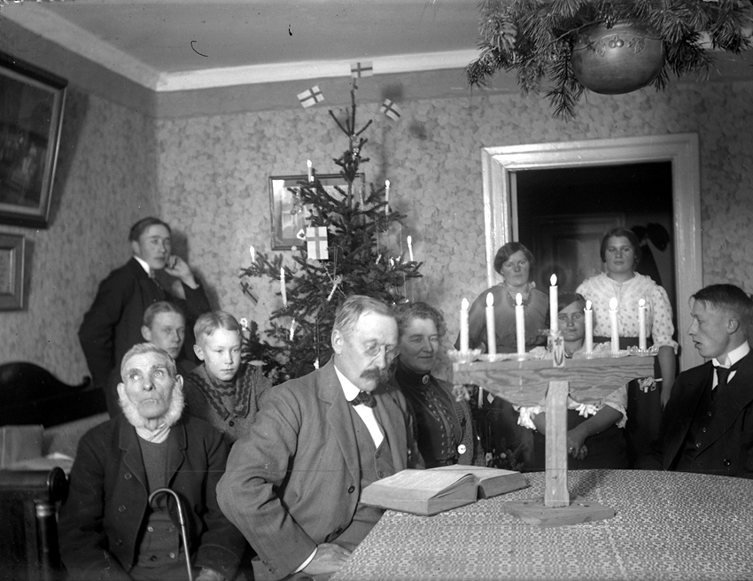 Familj firar jul med läsning av julevangeliet vid julgranen. Västerås.