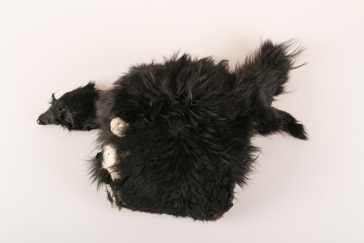 Muffe i svart pelsverk, med tillaget hode med falsk nese og øyne, samt hale. 