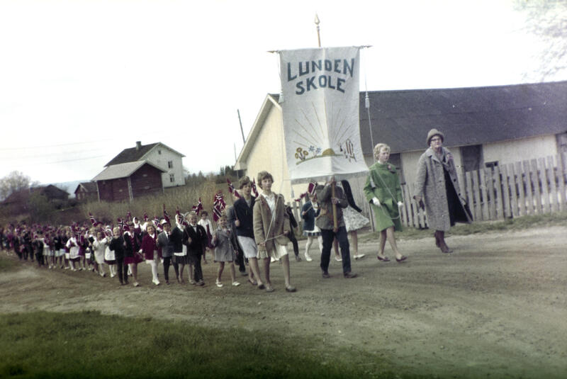 Fargebilde (blasse farger) av barnetog på 17. mai i Øvre Vang, fremst i toget bæres fana til Lunden skole.