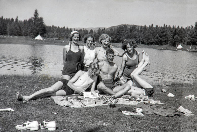 Gruppebilde av fire damer og tre menn som poserer nonchalant på badestranden en gang midt på 1900-tallet.