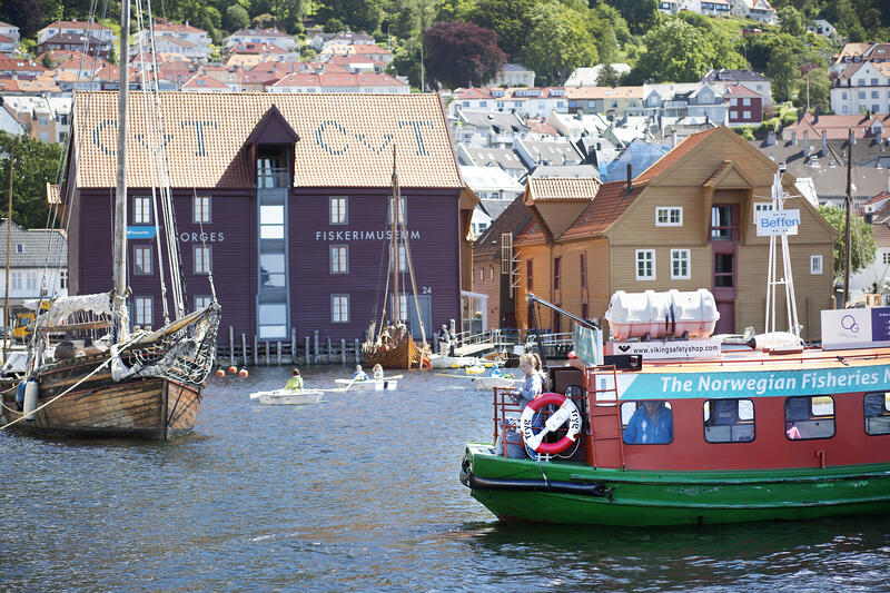 Her ser vi en aktiv havn, med flere robåter og Beffen som kommer inn til Norges Fiskerimuseum