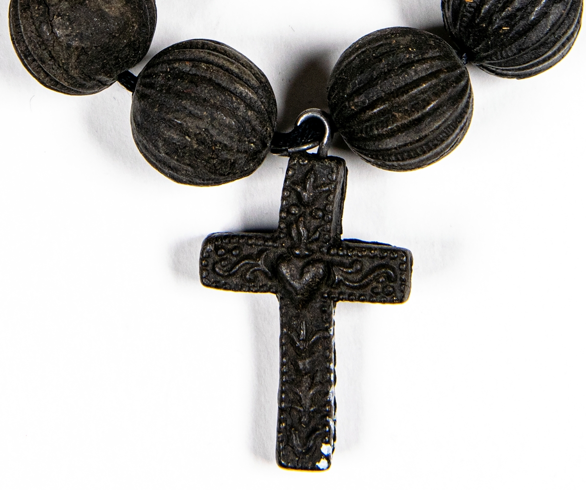 Armband av svarta kulor med räfflingar och med kors med hjärtan och andra motiv i relief. 
Sannolikt gjuten konstmassa såsom guttaperka.