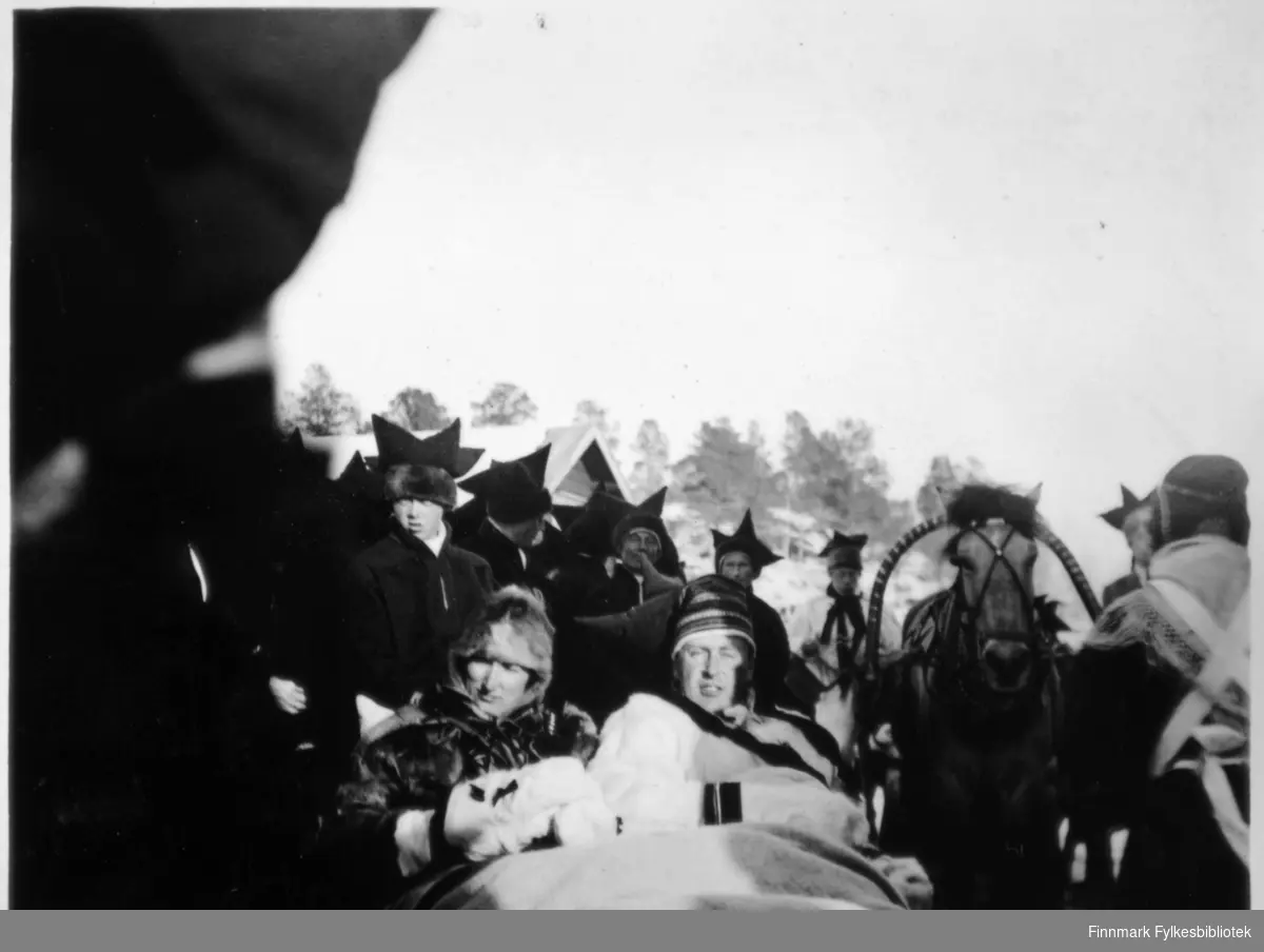 Bildet er tatt i Karasjok i forbindelse med kronprinsparet Olav og Märtha sin tur over Finnmarksvidda i påsken 1934. Olav og Märtha sitter i slede og de er kledd i pesk.
