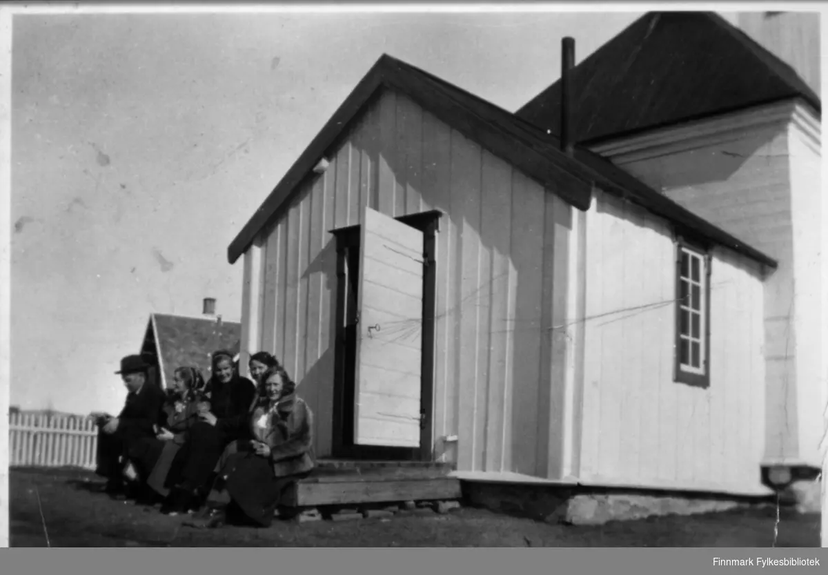 En mann og fire kvinner sitter på trappen til Karasjok kirke.