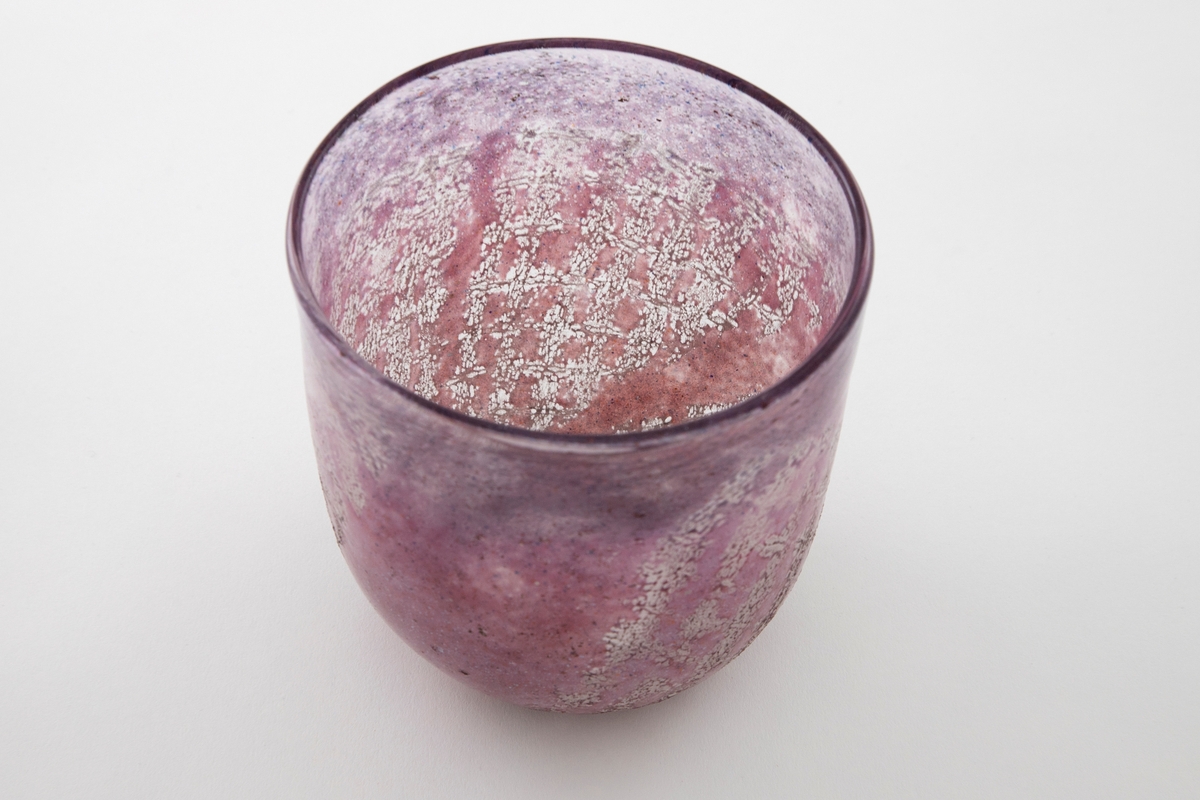 Tilnærmet sylindrisk bolle i halvgjennomskinnelig glass. Overflaten er dekorert med lilla og rødlig emaljefarge samt glassfiber, som danner et rutemønster på bollens nedre del.